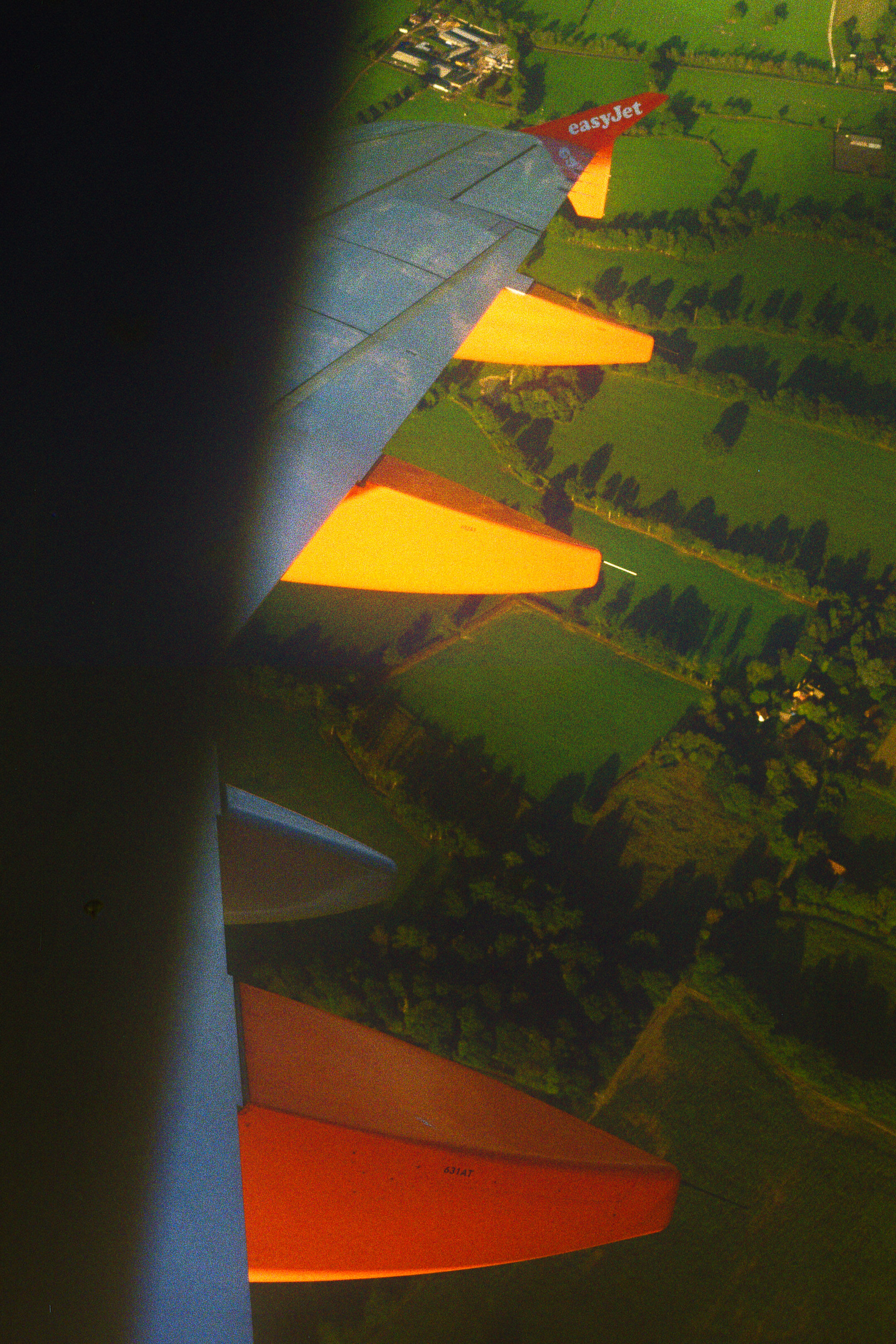 Airplane wing turning right and green fields below