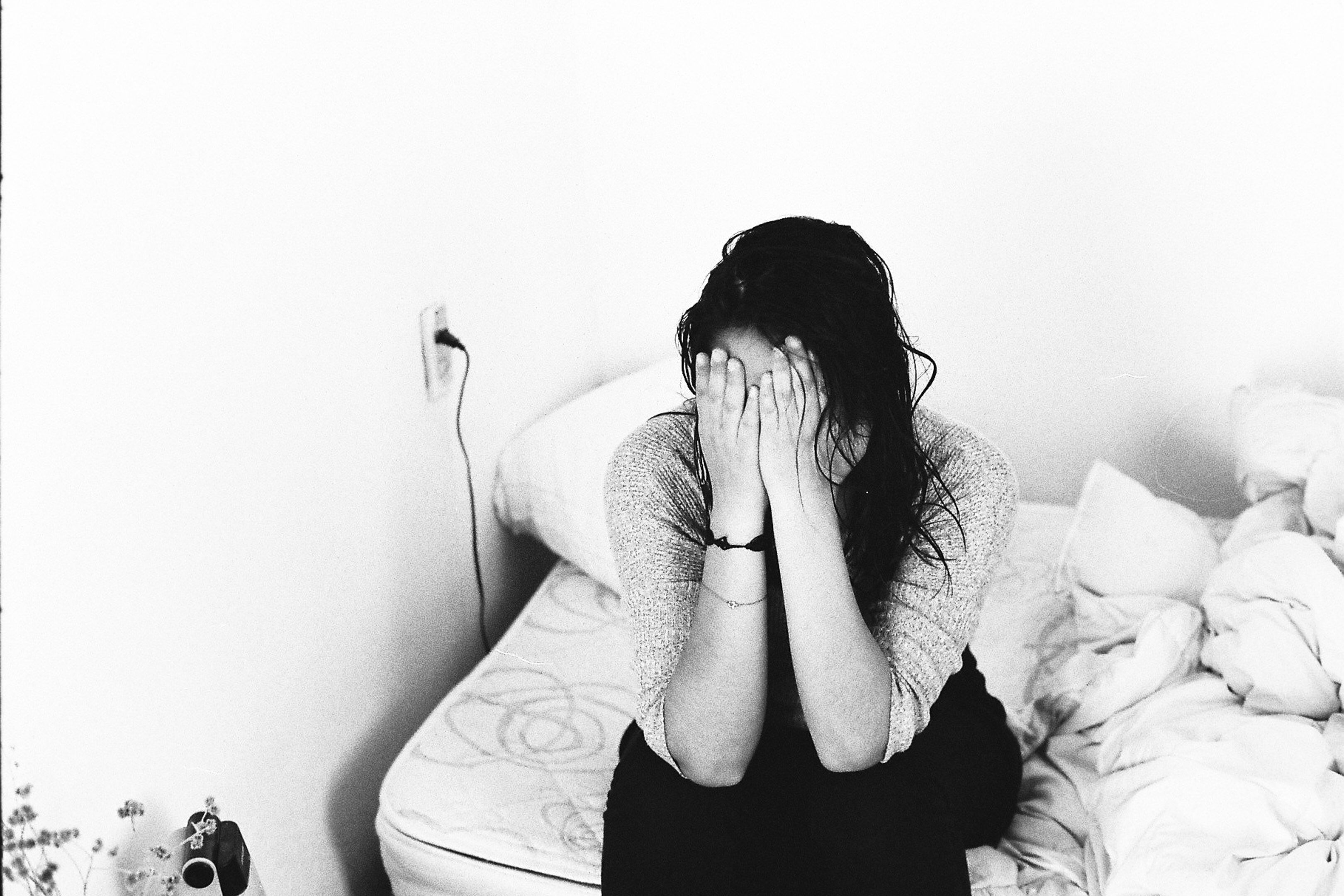 woman sitting on bed holding her hands in front of her face